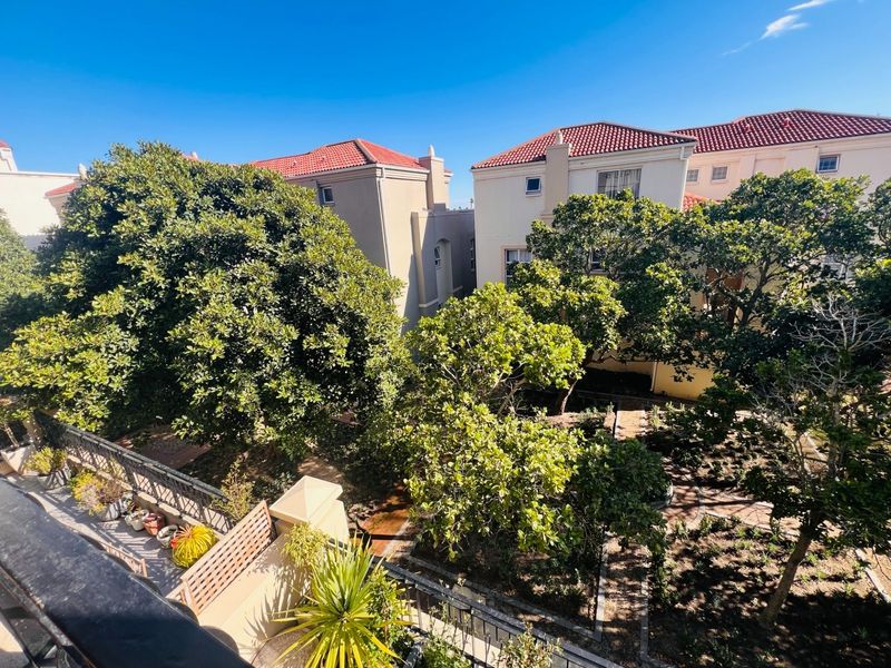 An elevated view overlooking a landscaped garden area with mature trees and paved pathways between residential apartment buildings.