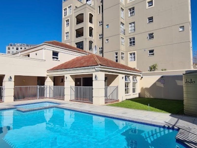 Communal swimming pool area featuring a paved deck, manicured lawn, and a water storage tank within an apartment complex setting.