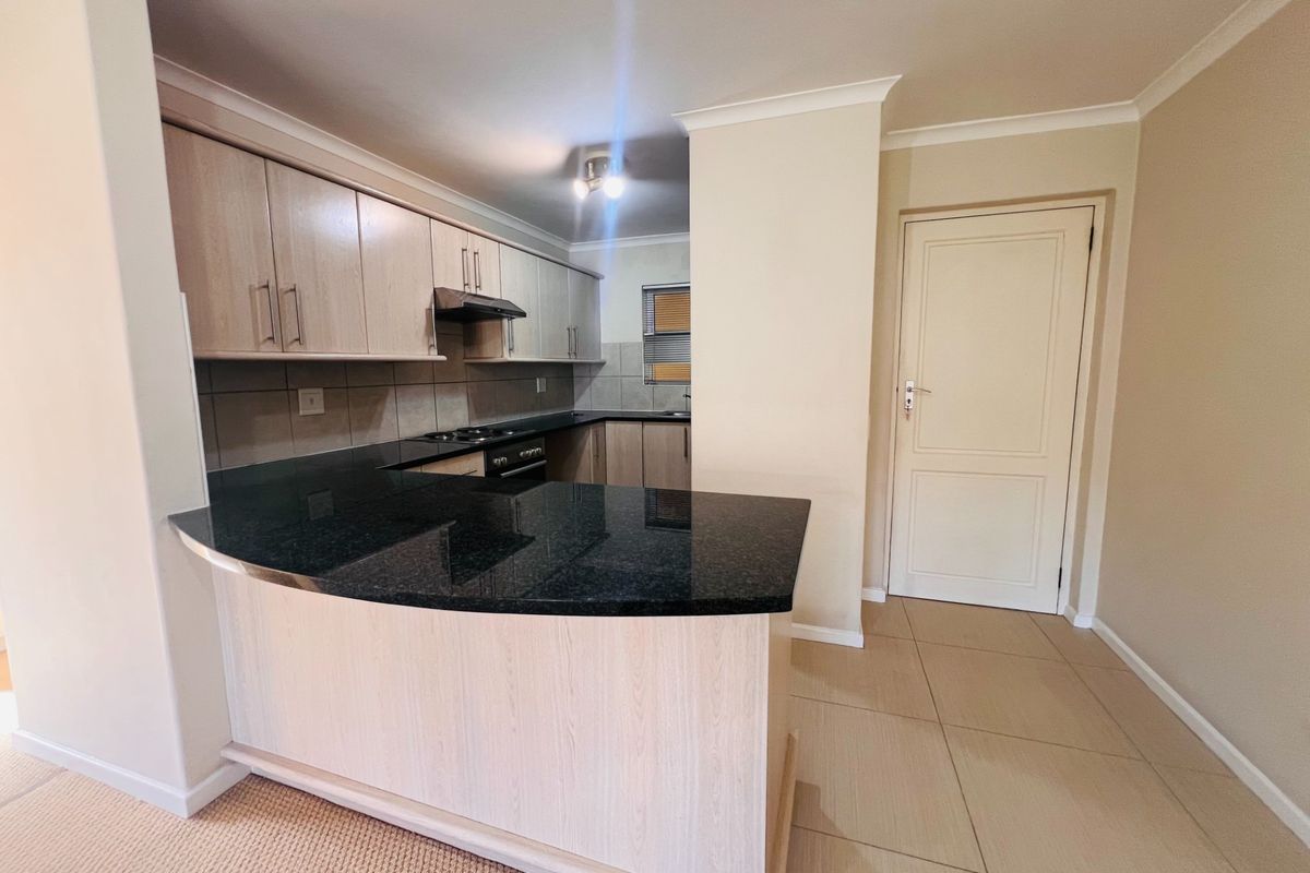 A functional kitchen featuring light wood cabinetry, dark granite countertops, a built-in hob, and an extractor fan, with tiled flooring throughout.