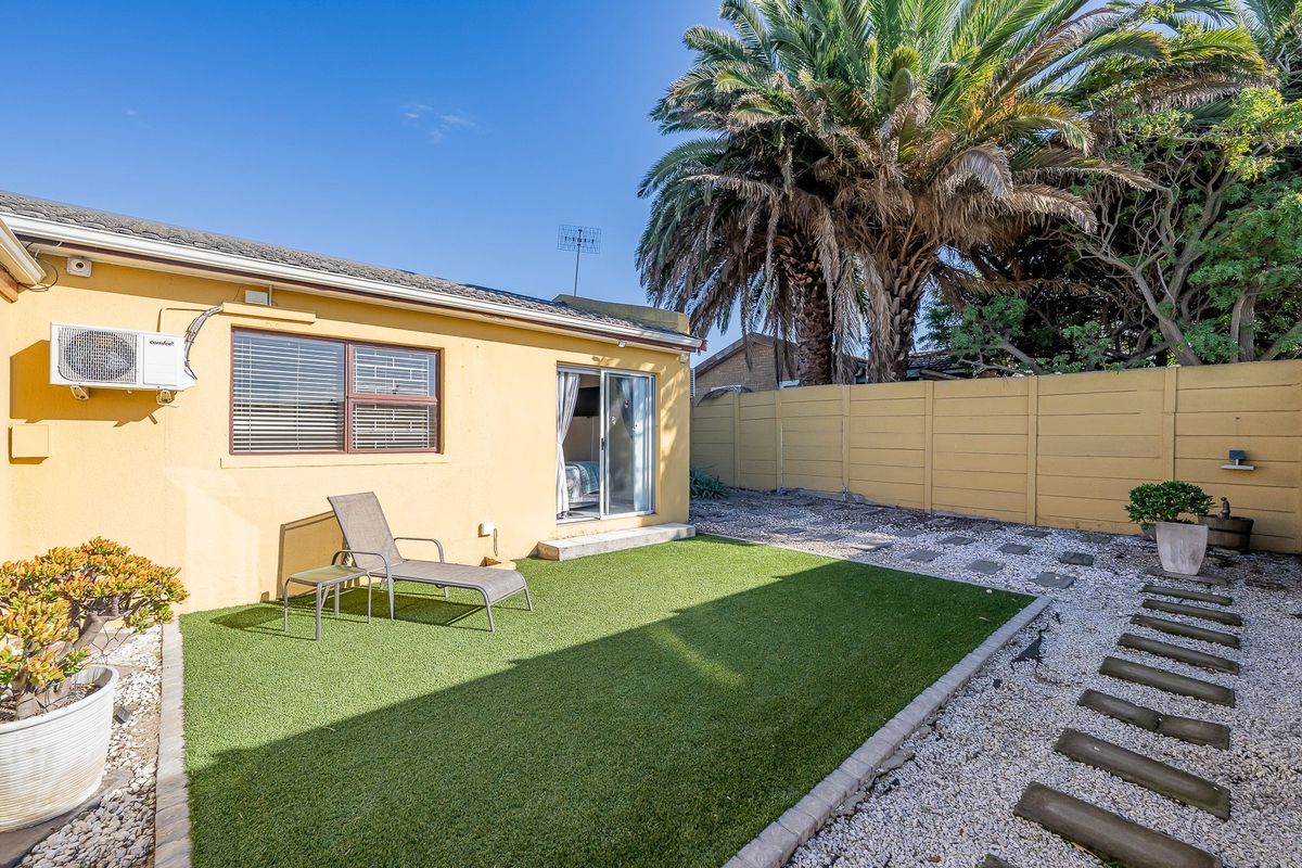 Rear exterior view featuring a low-maintenance garden with artificial turf, paved stepping stones, and a wall-mounted air conditioning unit.