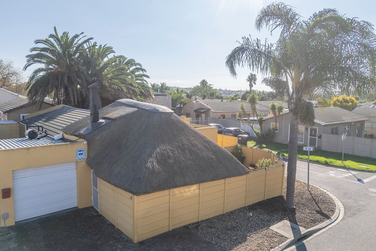 Aerial view of a corner property featuring a distinctive thatched roof, attached garage, and perimeter walling in a residential neighbourhood.