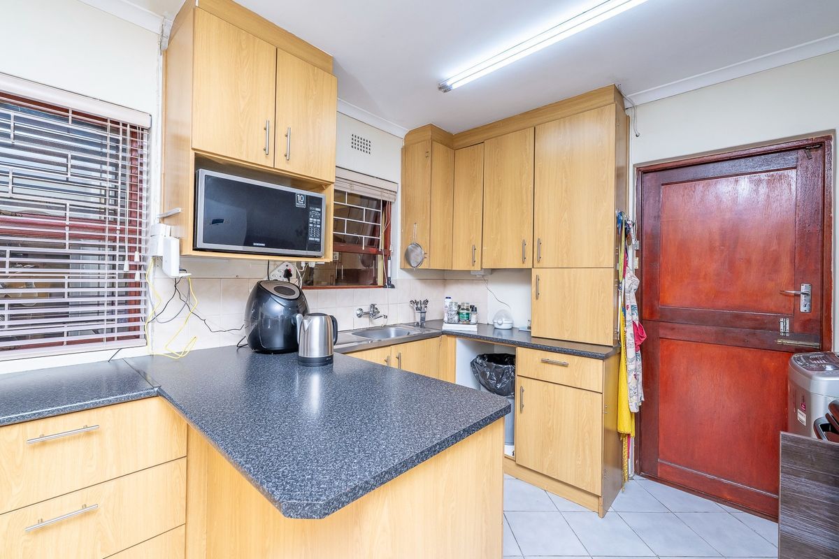 Functional kitchen featuring light wood cabinetry, dark laminate countertops, stainless steel sink, and tiled flooring with direct access to an exterior door.