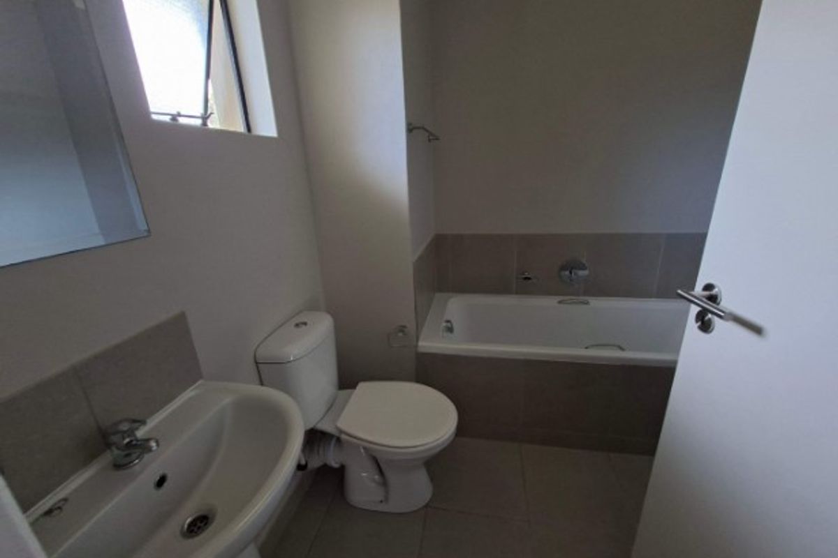A functional bathroom featuring a pedestal basin, a standard toilet, and a tiled bathtub with neutral wall and floor finishes.