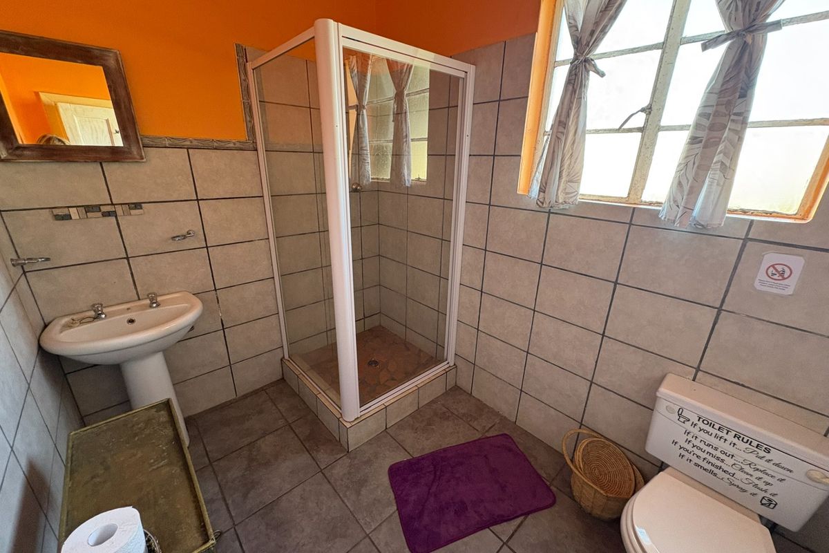 A functional bathroom featuring a corner shower enclosure, pedestal basin, and toilet with tiled walls and flooring.