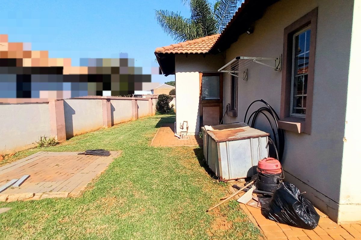 A rear exterior view of the property featuring a paved walkway, lawn area, and perimeter boundary wall.