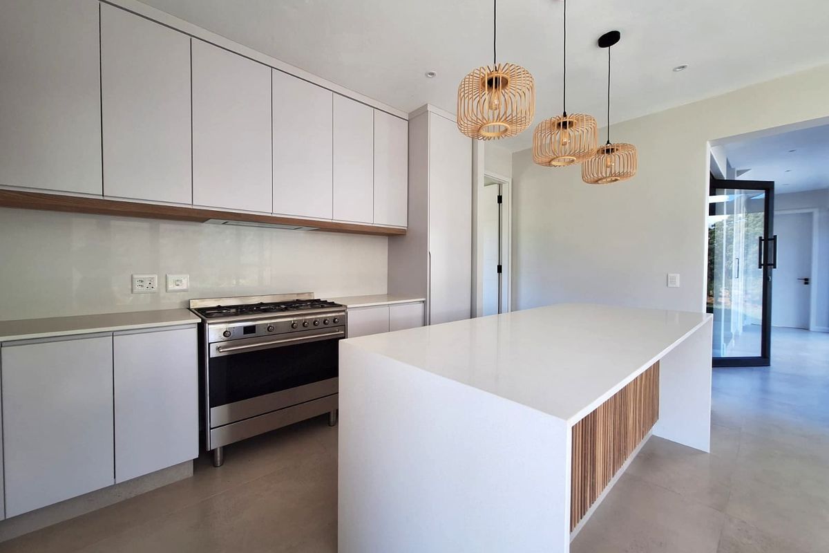 Modern kitchen featuring sleek white cabinetry, a central island with timber detailing, stone countertops, and a stainless steel gas range.