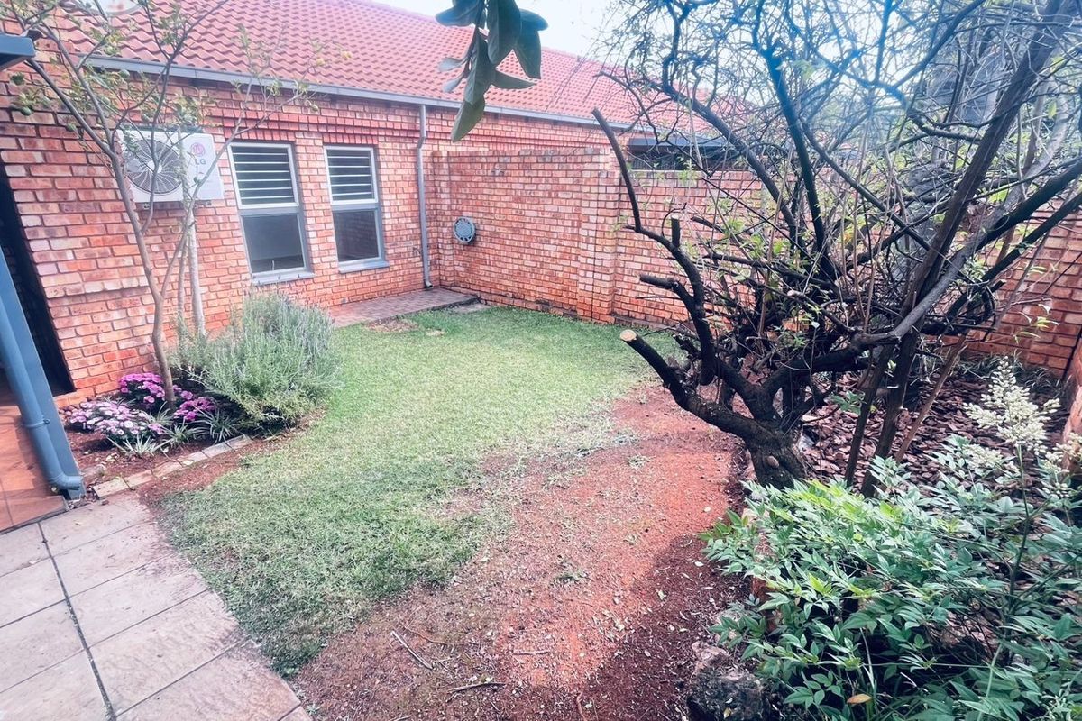 A private rear courtyard featuring a brick-walled perimeter, paved patio area, and a small garden space with established trees and shrubs.