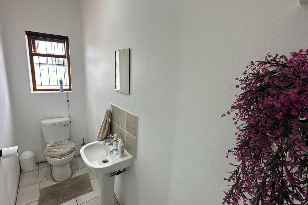 A functional office restroom featuring a pedestal basin, tiled splashback, and a standard toilet with a security-barred window.