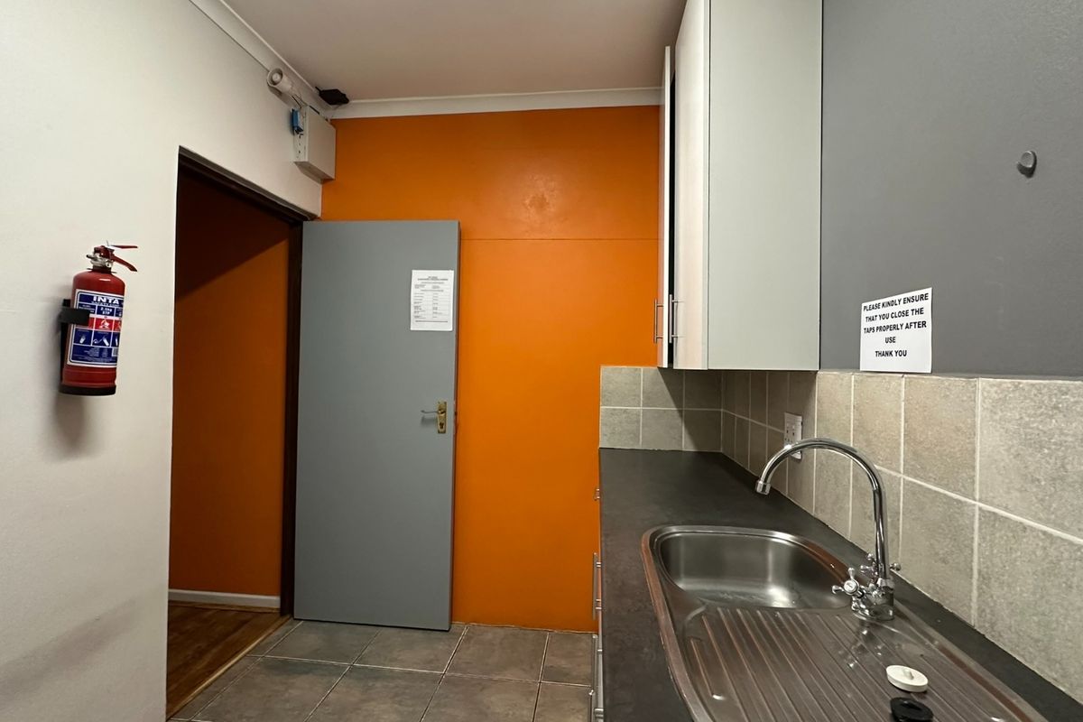 A functional office kitchenette featuring a stainless steel sink, tiled backsplash, and overhead cabinetry, equipped with a wall-mounted fire extinguisher.