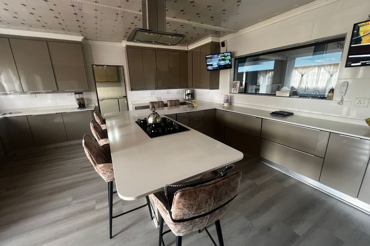 Modern kitchen featuring sleek cabinetry, a central island with a built-in cooktop, stainless steel extractor fan, and durable laminate flooring.