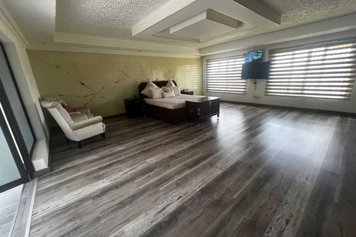 Spacious bedroom featuring modern wood-look flooring, a decorative tray ceiling with recessed lighting, and large windows with fitted blinds.