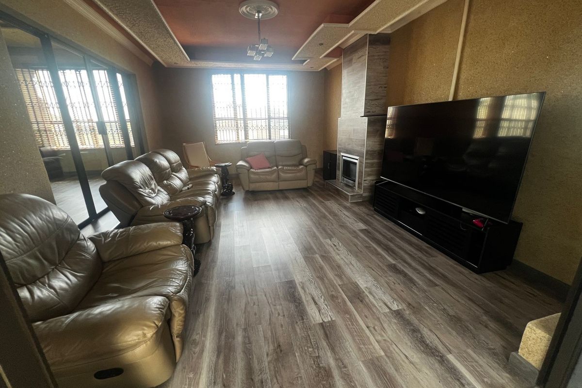 Spacious living room featuring wood-look laminate flooring, a built-in fireplace with stone-effect cladding, and a decorative tray ceiling with recessed lighting.