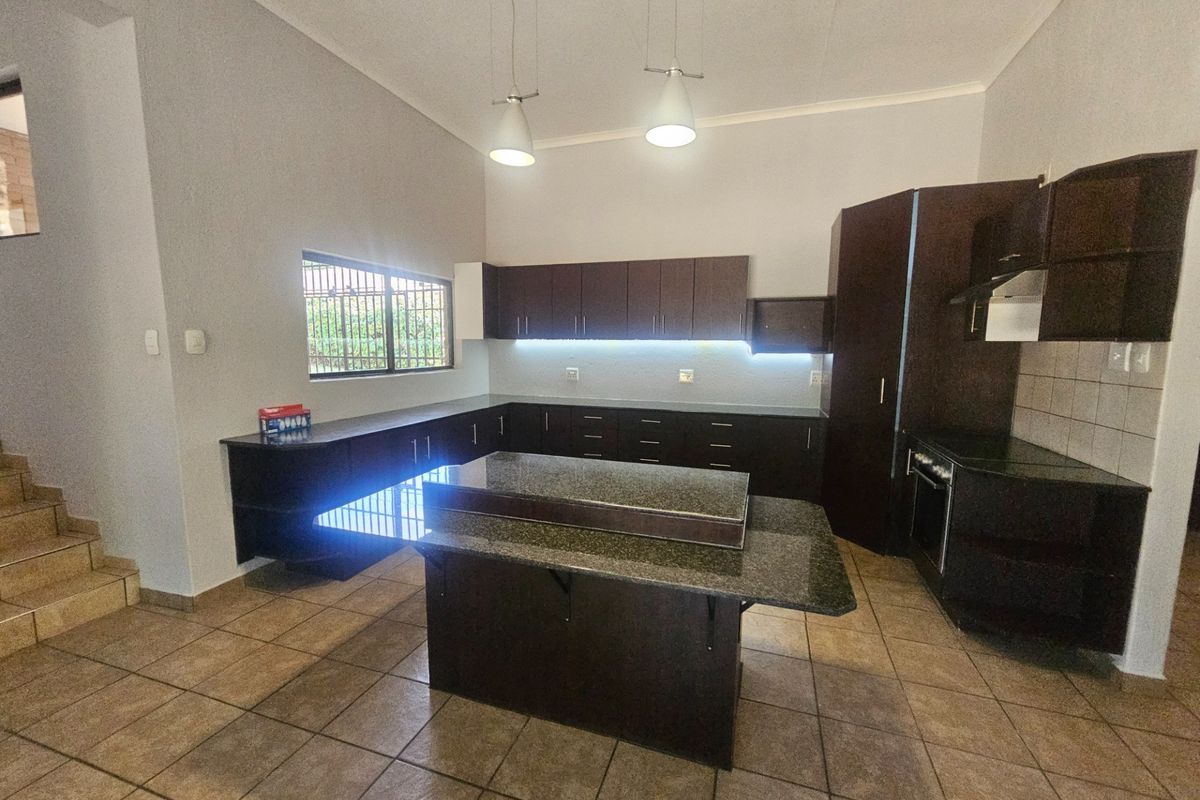 Modern kitchen featuring dark cabinetry, granite countertops, a central island, built-in oven, and tiled flooring with under-cabinet lighting.