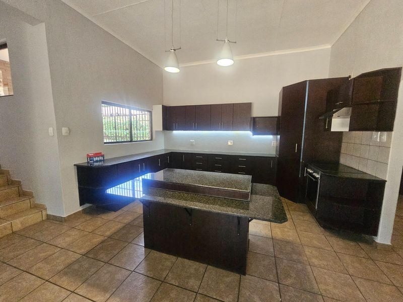Modern kitchen featuring dark cabinetry, granite countertops, a central island, built-in oven, and tiled flooring with under-cabinet lighting.