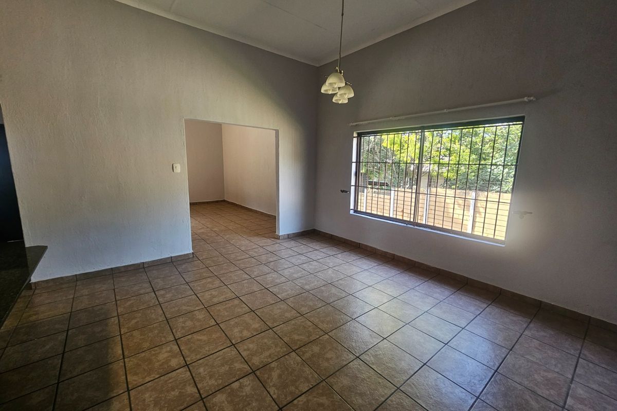 An empty living area featuring tiled flooring, a large window with security bars, and a central pendant light fixture.
