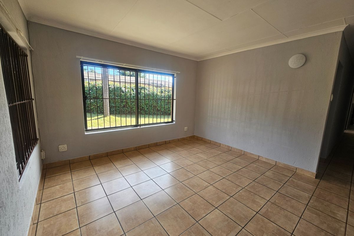 A vacant bedroom featuring neutral grey walls, tiled flooring, and a large window fitted with security bars.