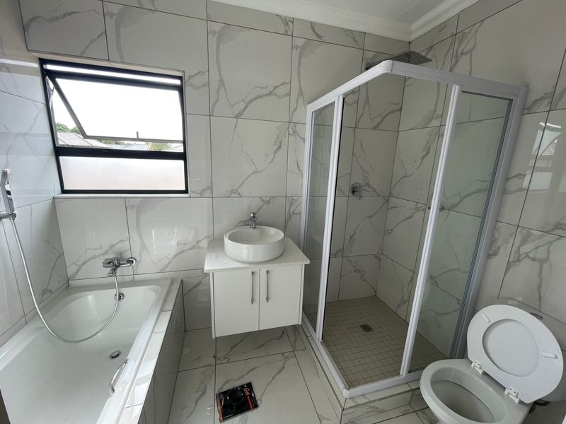 Modern bathroom featuring marble-look wall and floor tiles, a built-in bathtub, a separate shower enclosure, and a wall-mounted vanity with a vessel sink.