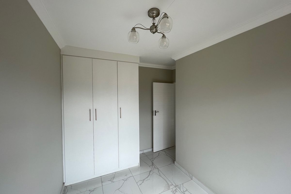 A clean, empty bedroom featuring modern marble-look floor tiles, neutral wall paint, and a built-in wardrobe with contemporary finishes.