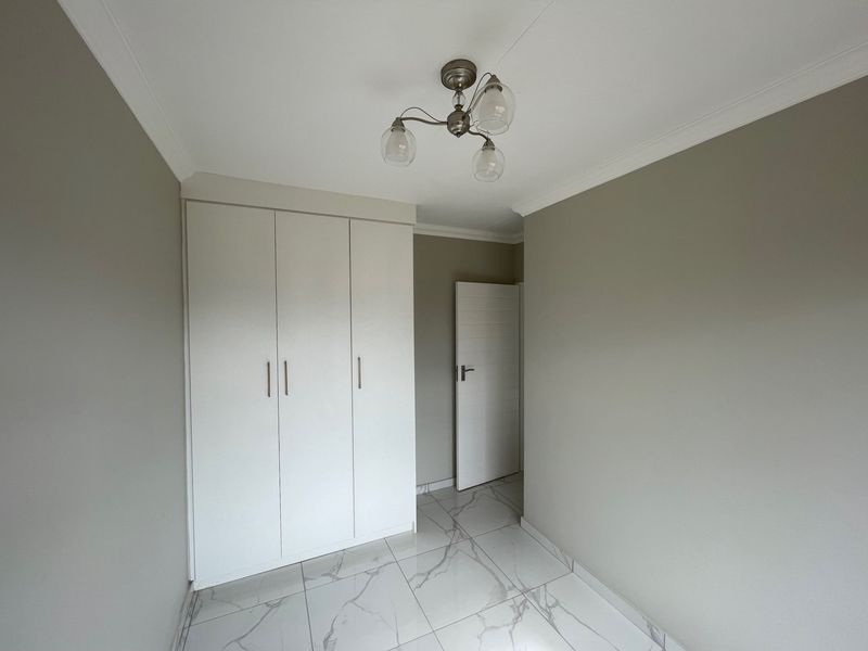 A clean, empty bedroom featuring modern marble-look floor tiles, neutral wall paint, and a built-in wardrobe with contemporary finishes.