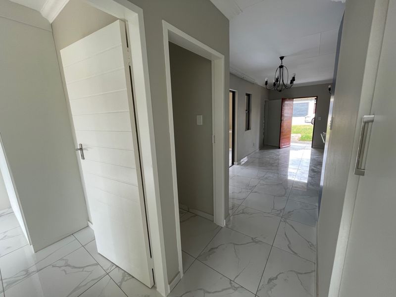 A bright, modern hallway featuring large-format marble-look floor tiles, neutral wall finishes, and clean architectural lines leading toward an exterior entrance.
