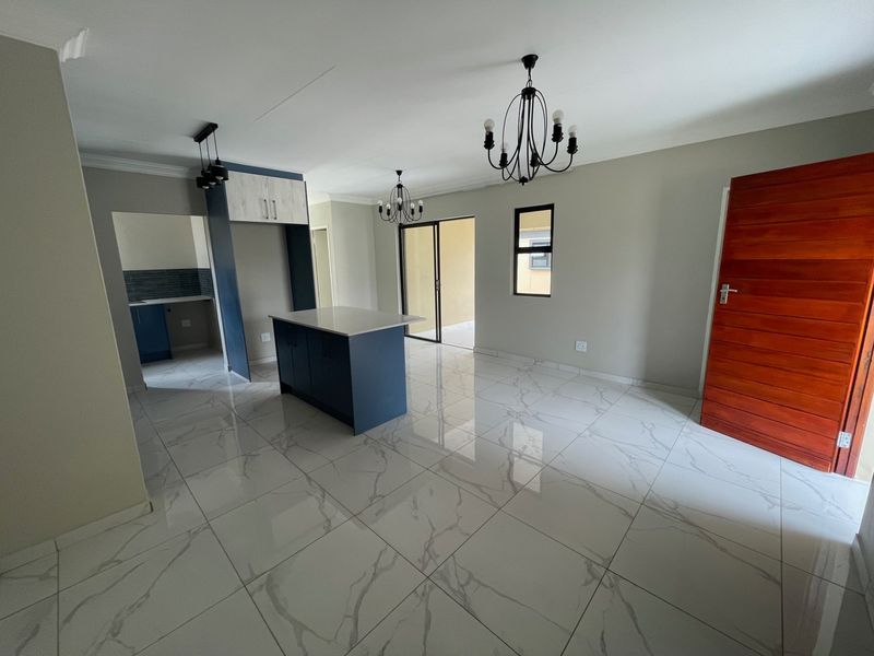 Modern open-plan living area featuring high-gloss marble-look floor tiles, a central kitchen island with blue cabinetry, and direct access to an outdoor patio.