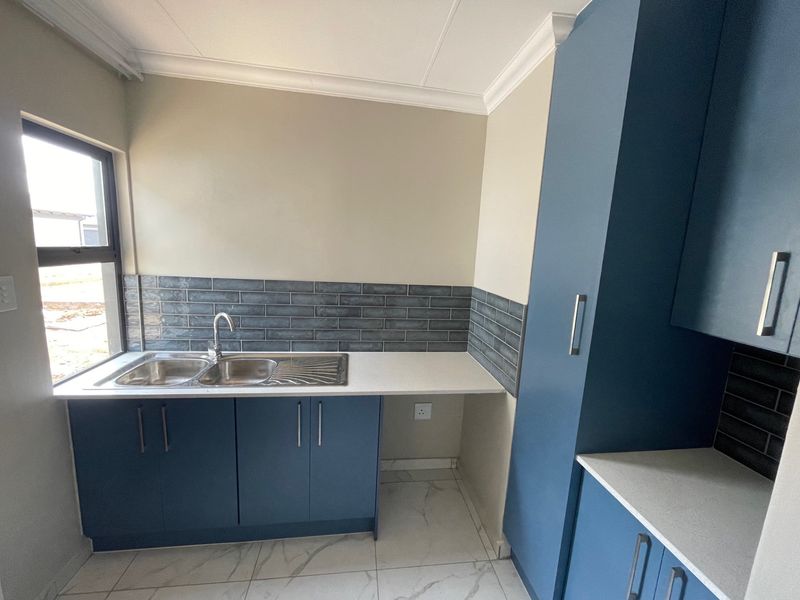 A modern, clean kitchen featuring blue cabinetry, quartz countertops, a double bowl stainless steel sink, and stylish subway tile backsplash.
