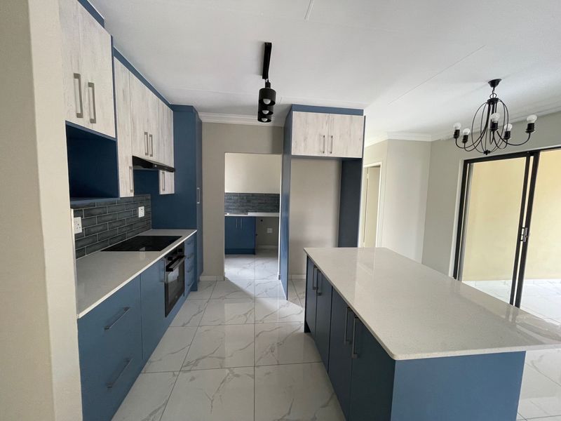 Modern kitchen featuring blue and wood-grain cabinetry, stone countertops, a central island, and high-quality tiled flooring with direct access to the patio.