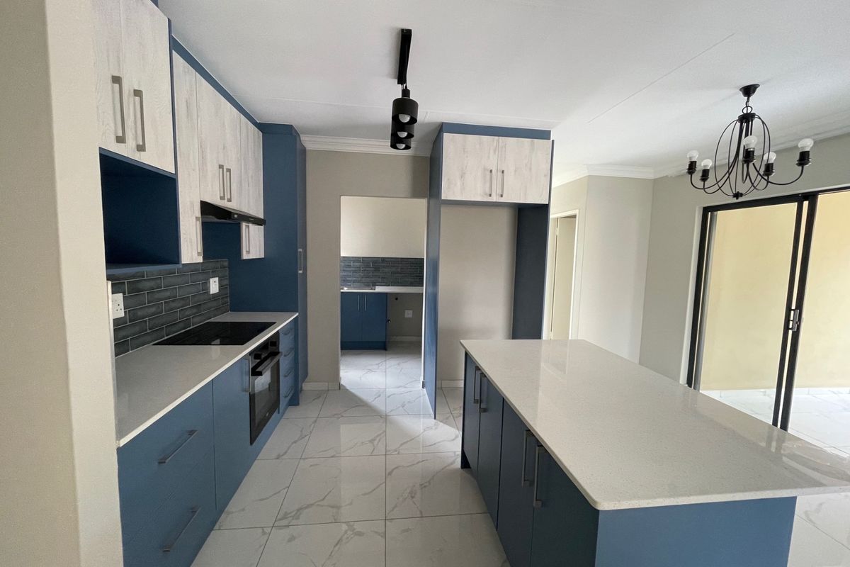 Modern kitchen featuring blue and wood-grain cabinetry, stone countertops, a central island, and high-quality tiled flooring with direct access to the patio.
