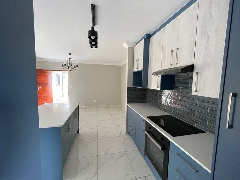 Modern kitchen featuring blue and wood-grain cabinetry, stone countertops, integrated appliances, subway tile backsplash, and large-format marble-look floor tiles.