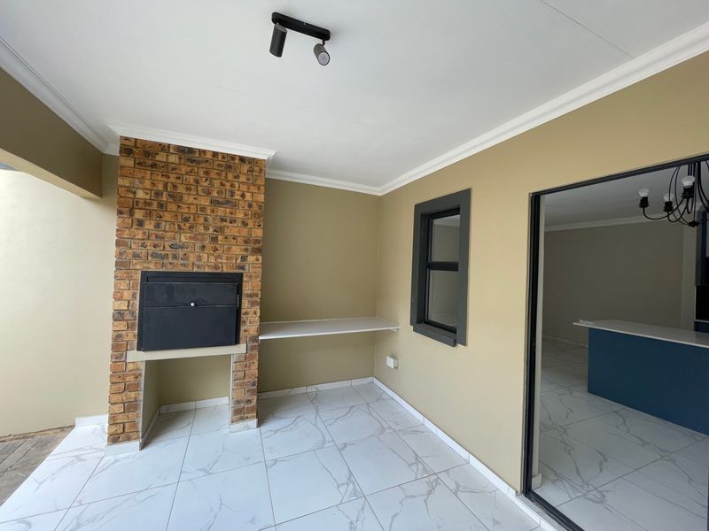 Covered patio area featuring a built-in brick braai, modern marble-look tiled flooring, and direct access to the interior living space.