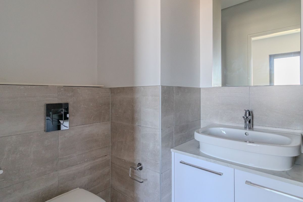 A modern bathroom featuring a wall-mounted toilet, a sleek vanity with a countertop basin, and neutral wall tiling.