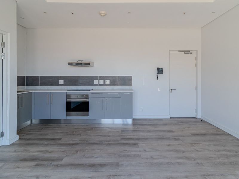 Modern open-plan kitchen featuring grey cabinetry, integrated oven, hob, and extractor fan, set against a neutral interior with wood-look flooring.