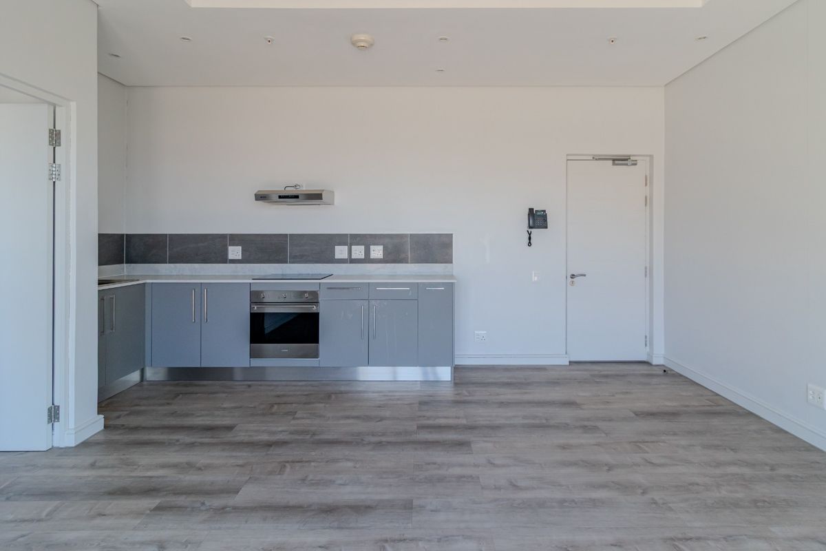 Modern open-plan kitchen featuring grey cabinetry, integrated oven, hob, and extractor fan, set against a neutral interior with wood-look flooring.