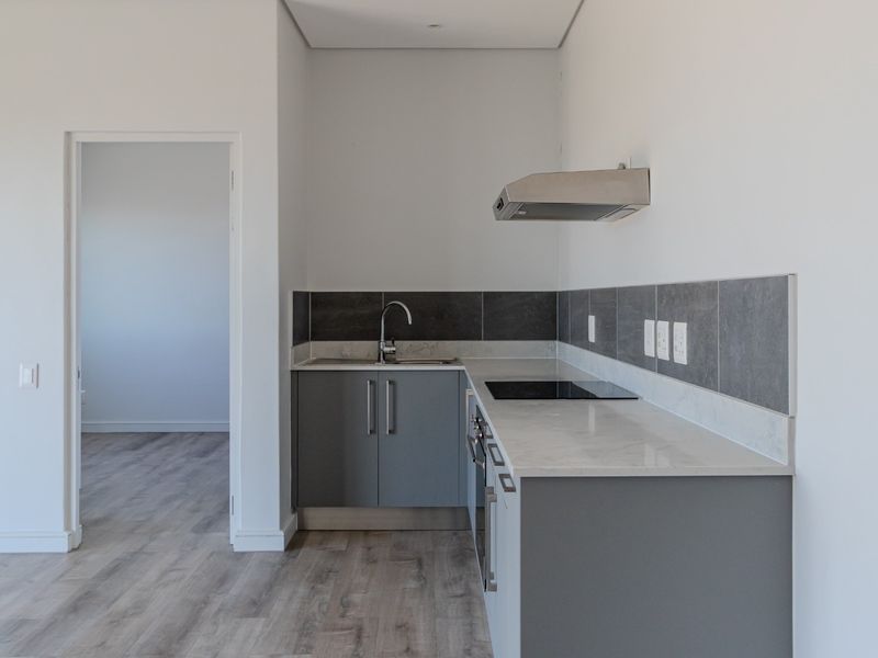 Modern kitchen featuring grey cabinetry, stone-look countertops, integrated electric hob, and stainless steel extractor fan, set within an open-plan living area.