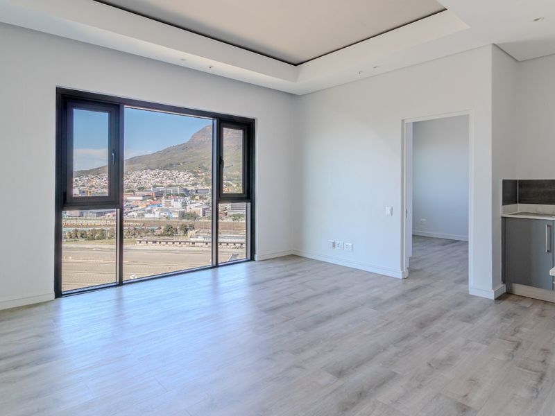 Modern open-plan living area featuring light wood-look flooring, recessed ceiling lighting, and a sleek kitchen with mountain and city views through large windows.