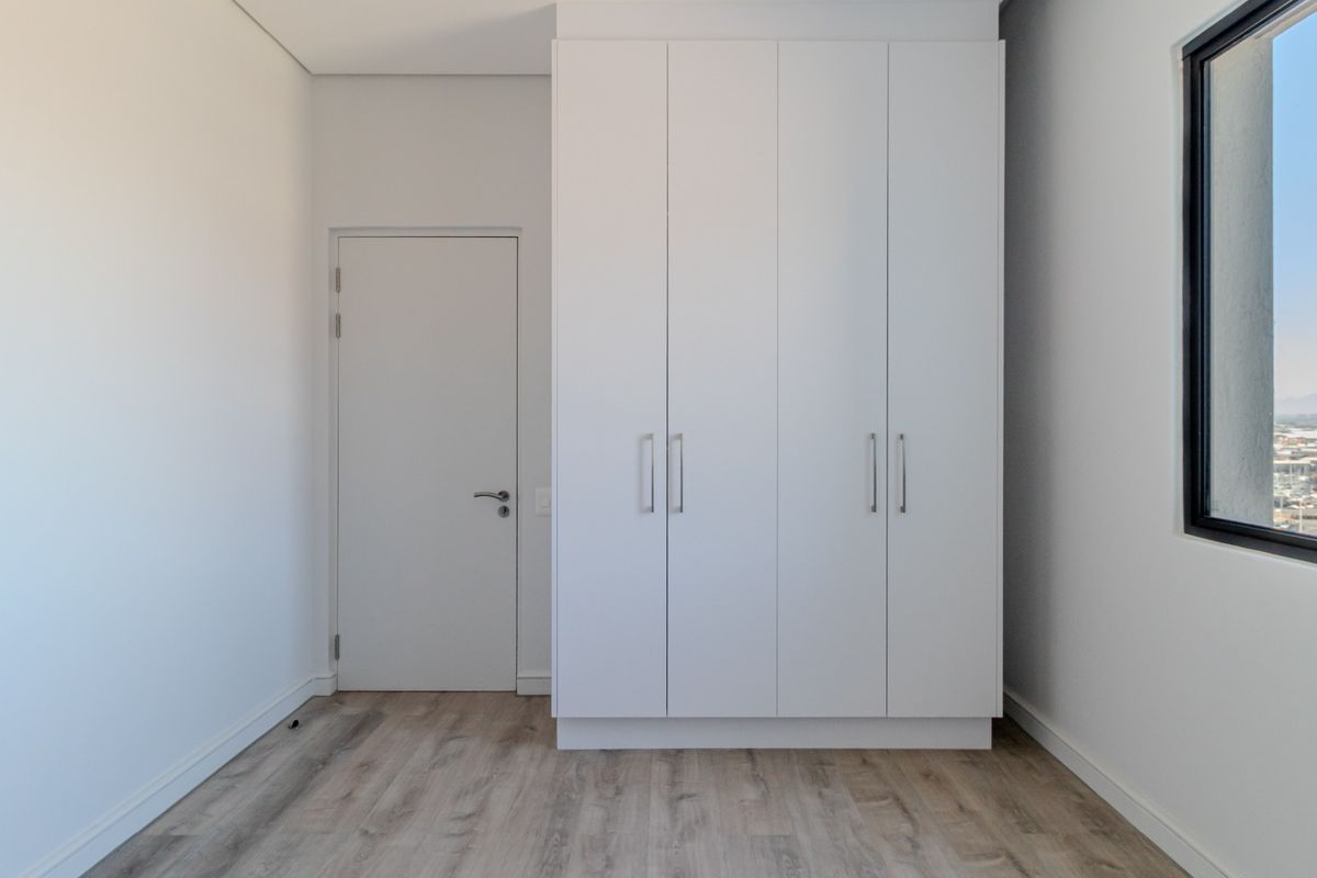 A bright, modern bedroom featuring built-in white cabinetry, light wood-look flooring, and a large window offering expansive views.