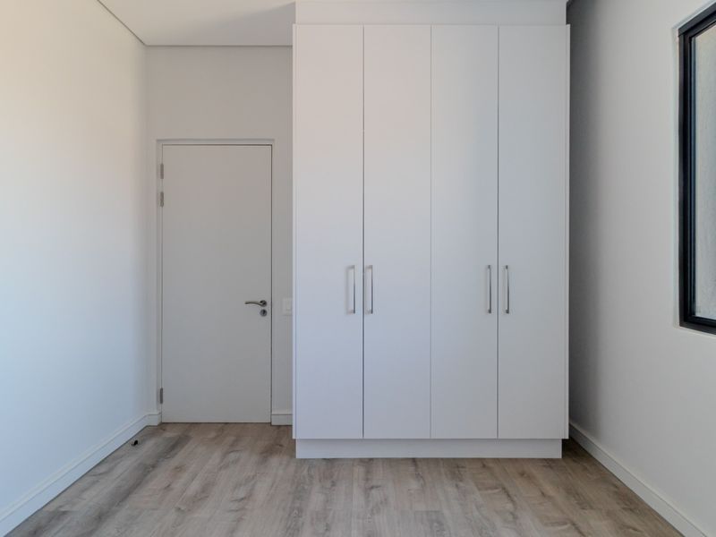 A bright, modern bedroom featuring built-in white cabinetry, light wood-look flooring, and a large window offering expansive views.