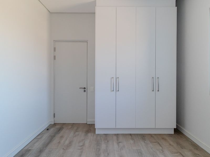 A bright, modern bedroom featuring light wood-look flooring, crisp white walls, and a large, built-in floor-to-ceiling wardrobe with sleek handles.