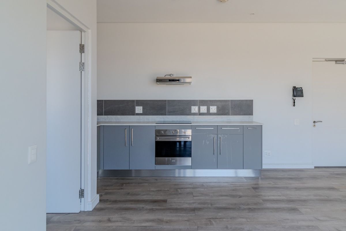 A modern, minimalist kitchen featuring grey cabinetry, a built-in oven, extractor fan, and sleek tiled backsplash, set within an open-plan living space.