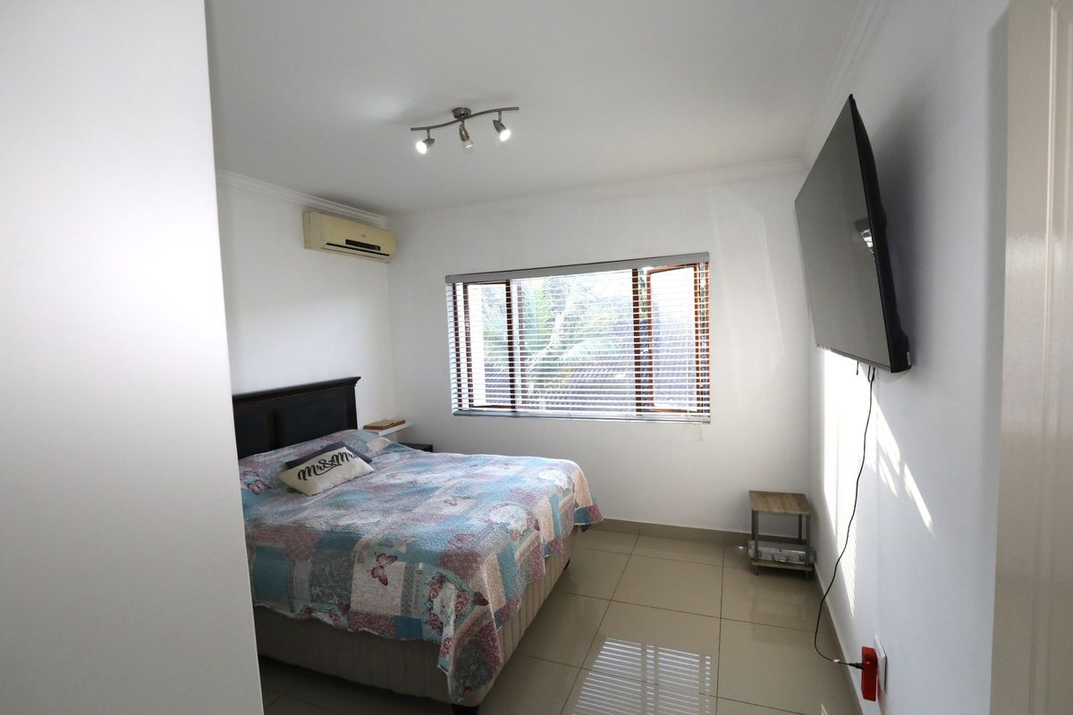 A functional bedroom featuring tiled flooring, a wall-mounted air conditioning unit, and a window with fitted blinds.