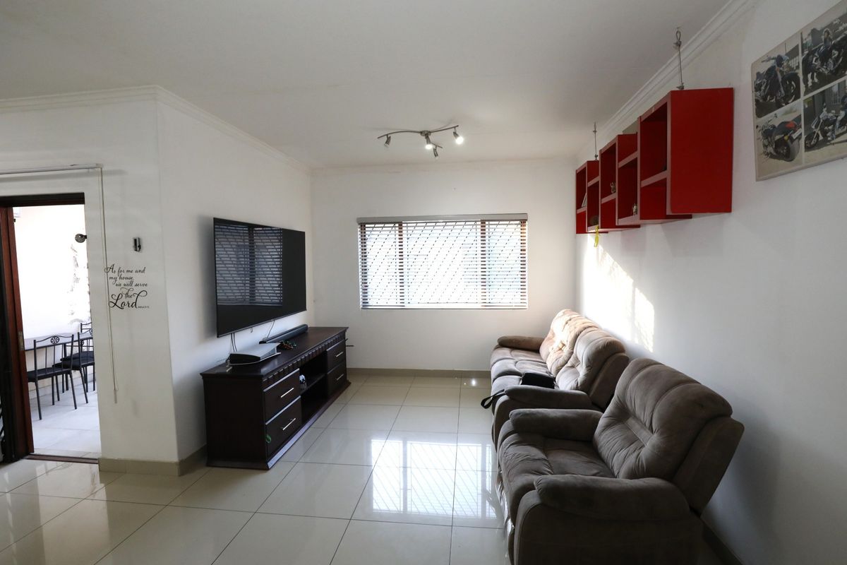 A well-lit living room featuring tiled flooring, a window with fitted blinds, and wall-mounted shelving, providing a comfortable and functional space.