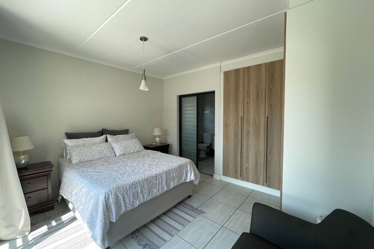 A well-maintained bedroom featuring built-in wooden cabinetry, tiled flooring, and an en-suite bathroom with a sliding door entrance.