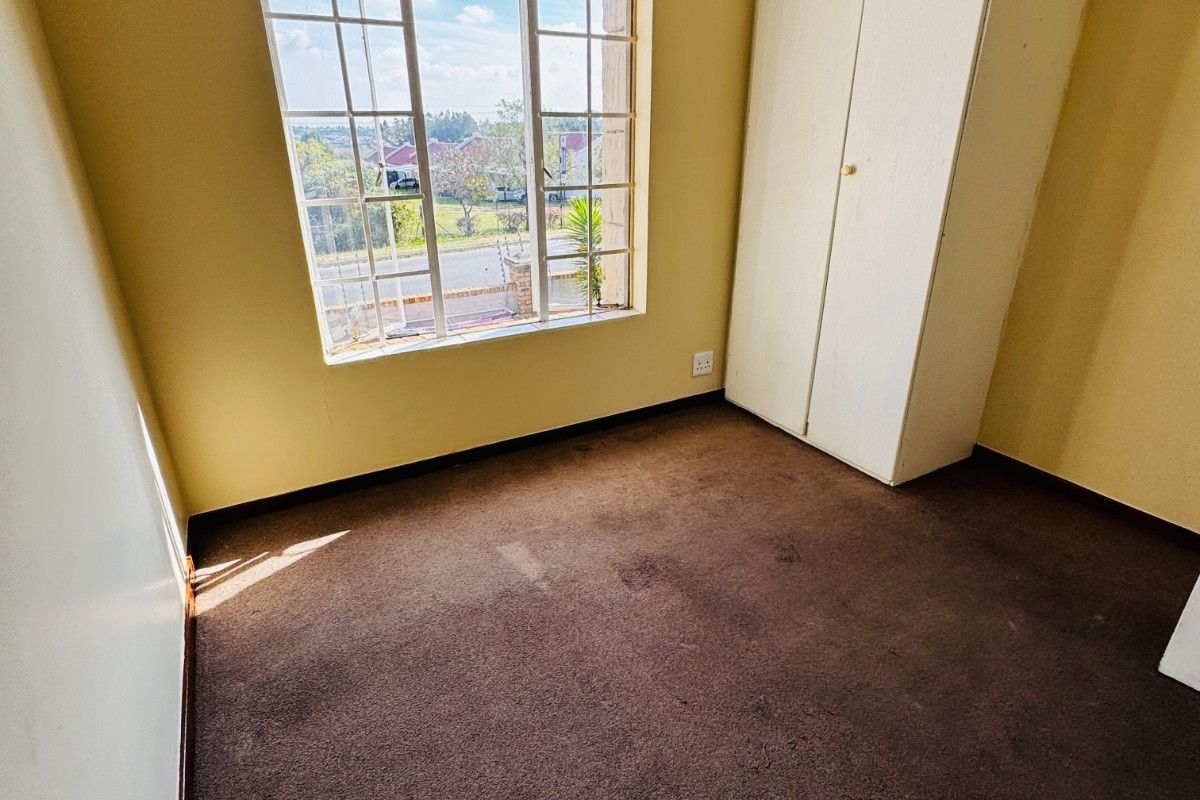 An empty bedroom featuring a built-in wardrobe, carpeted flooring, and a window with natural light.