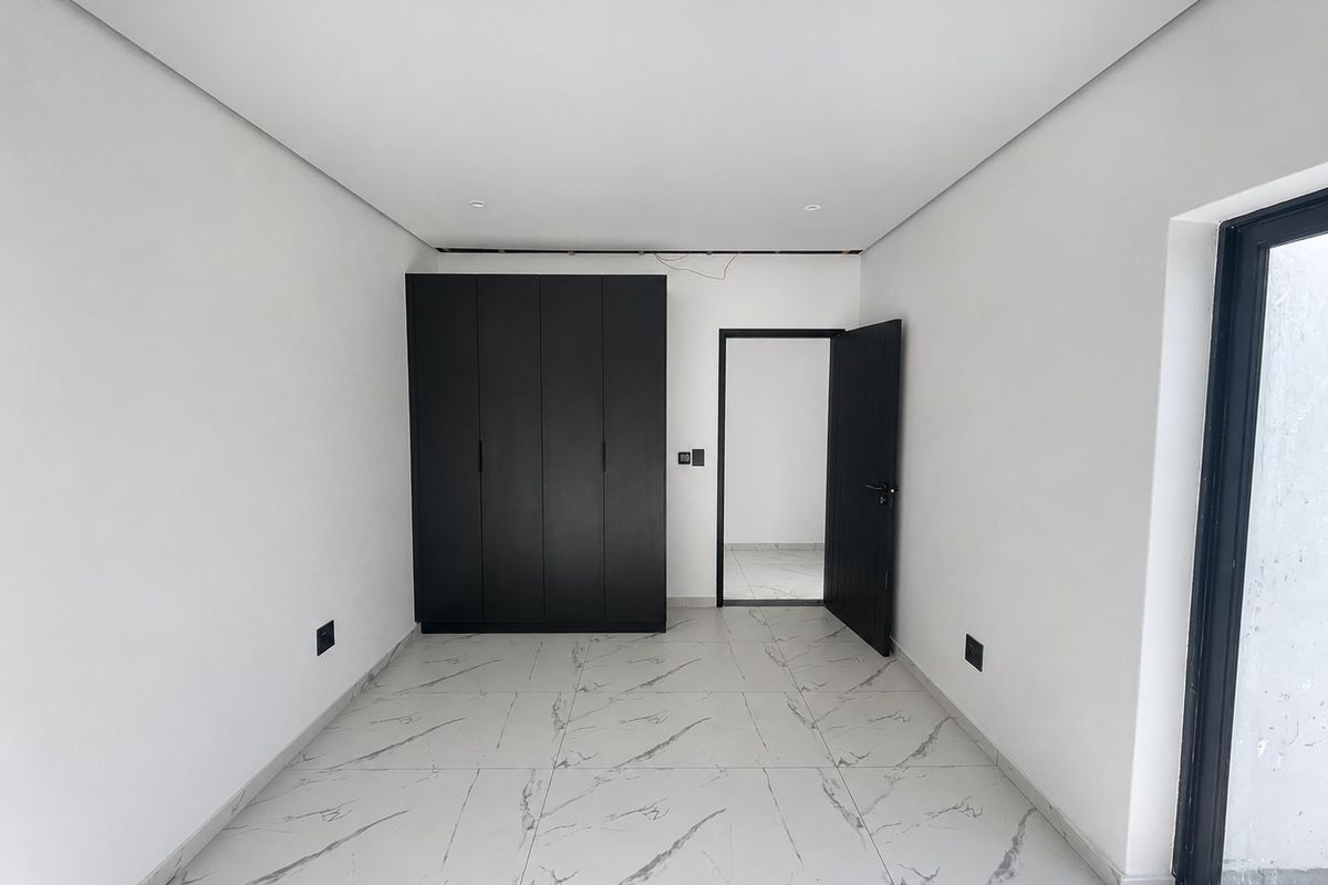A bright, modern bedroom featuring large-format marble-look floor tiles, built-in black cabinetry, and a minimalist aesthetic.
