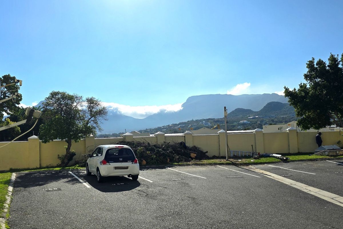 Exterior view of the apartment complex parking area featuring a boundary wall and scenic mountain backdrop.