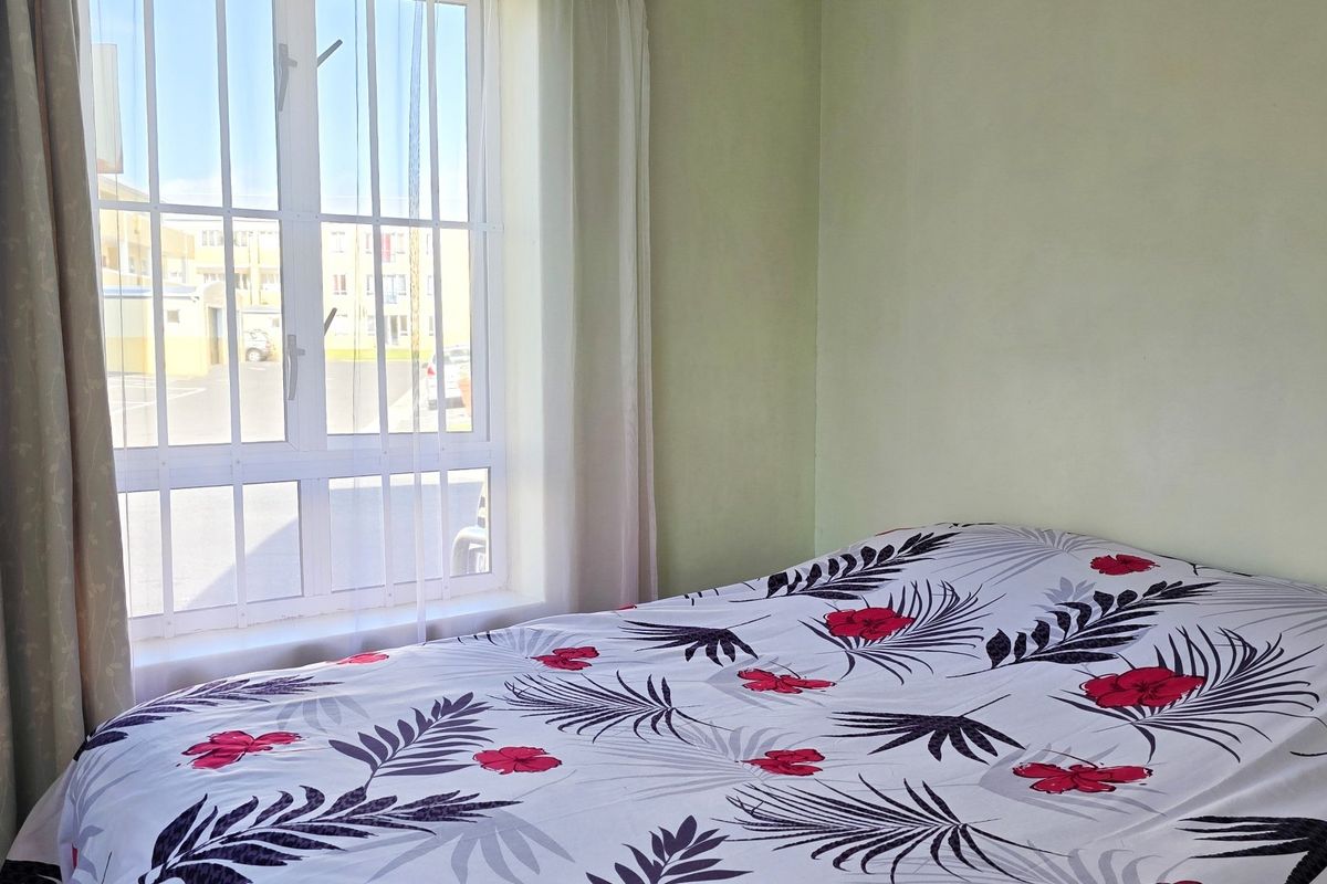 A bedroom featuring a window with integrated security bars, providing natural light and a view of the exterior complex area.