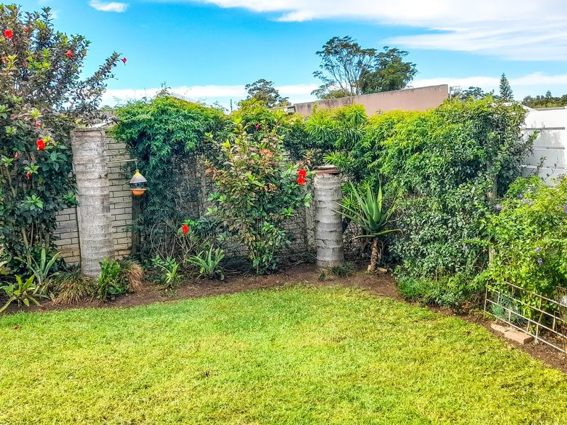 A private rear garden featuring a manicured lawn, established perimeter hedging, and brick boundary walling.