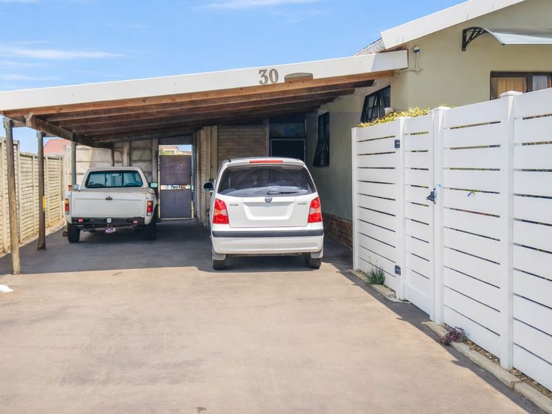 A paved driveway featuring a covered carport structure and white horizontal slat fencing, providing secure off-street parking.