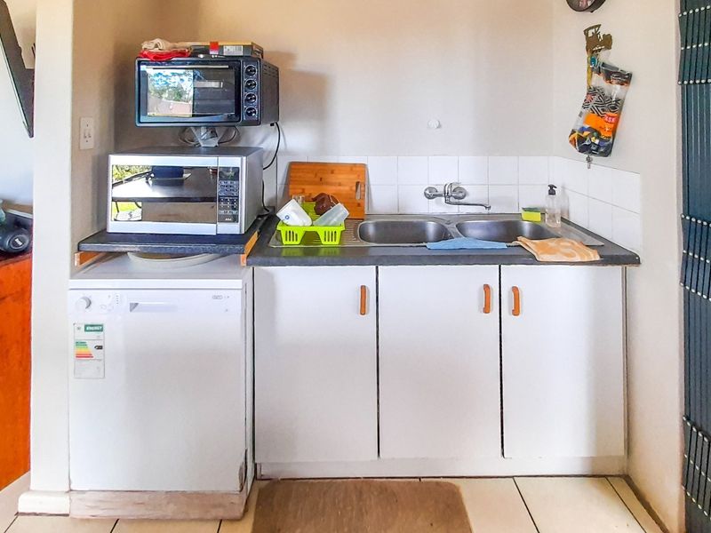 A compact scullery area featuring a double-basin sink, tiled splashback, and built-in cabinetry with space for a dishwasher.