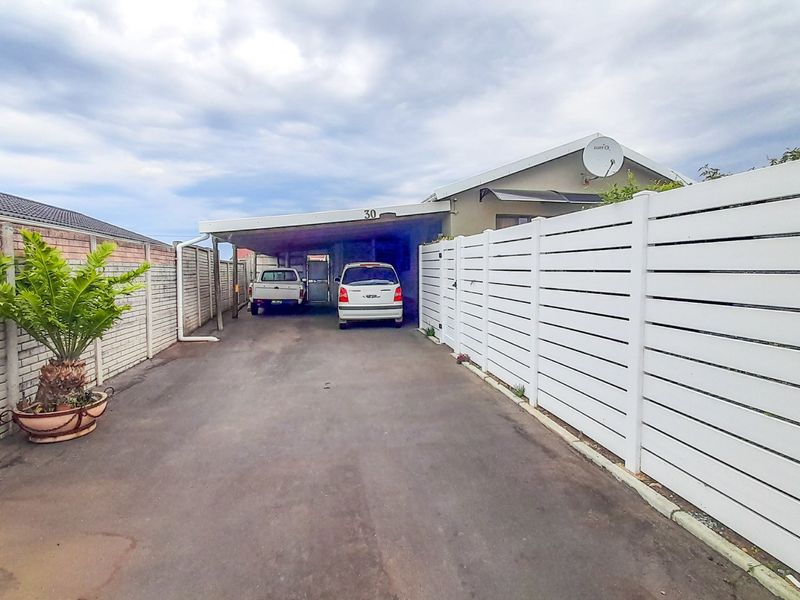 Front exterior view of the property featuring a paved driveway, covered carport, and white horizontal slat fencing.